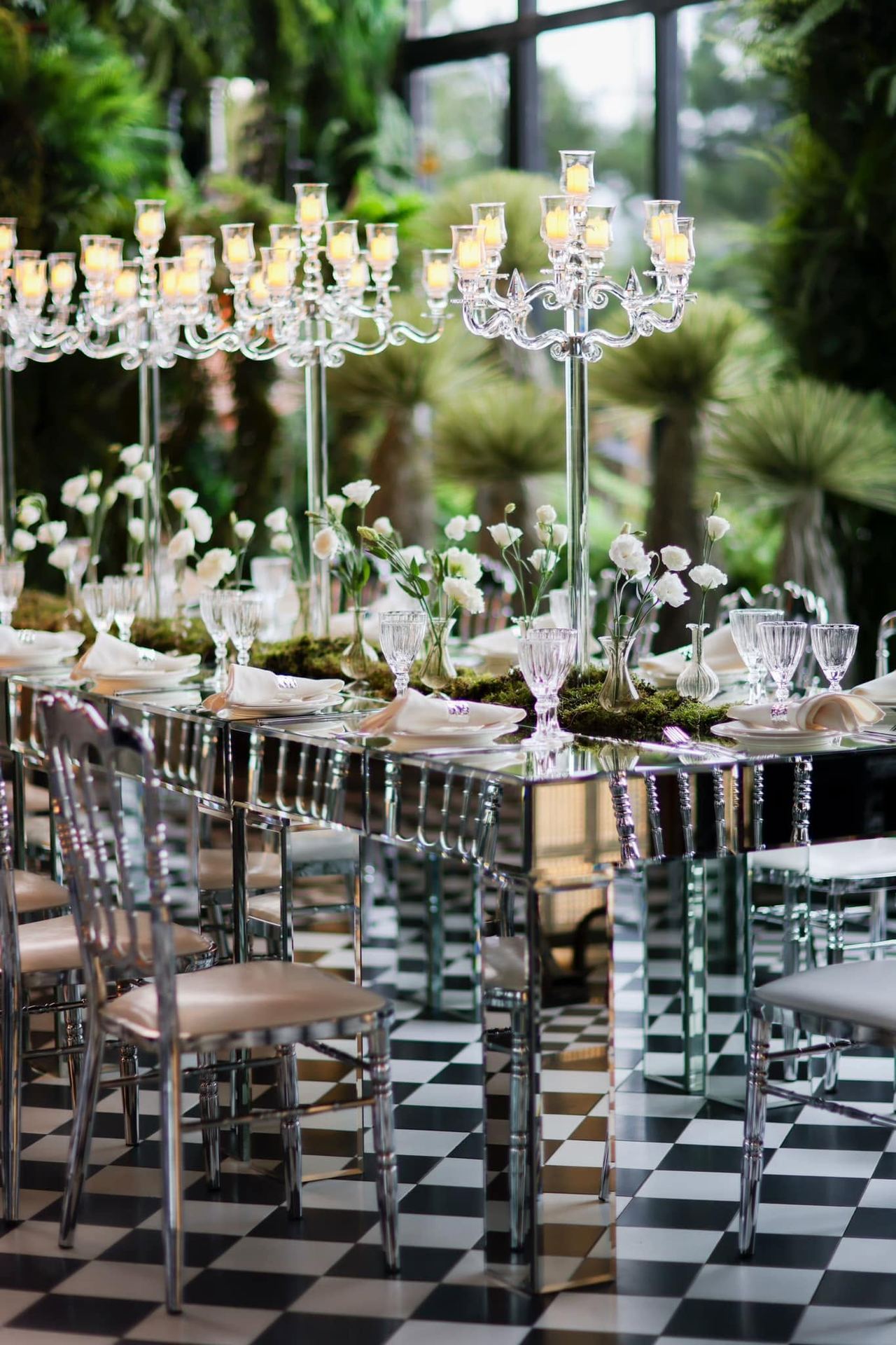 Candelabra table setting on a checkered floor surrounded by greenery